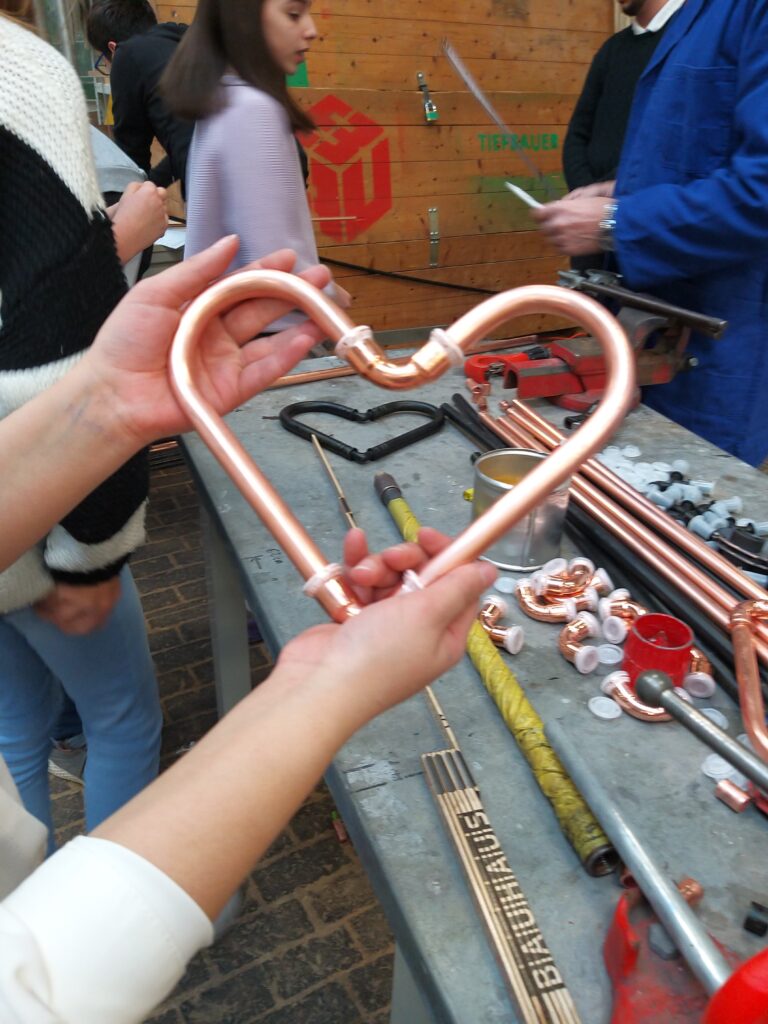 Hände einer Teilnehmerin zeigen ein selbstgebautes Herz aus Metall-Rohren