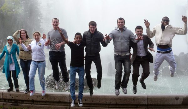 Kursteilnehmer springen vor einem Brunnen von einer Mauer in die Luft